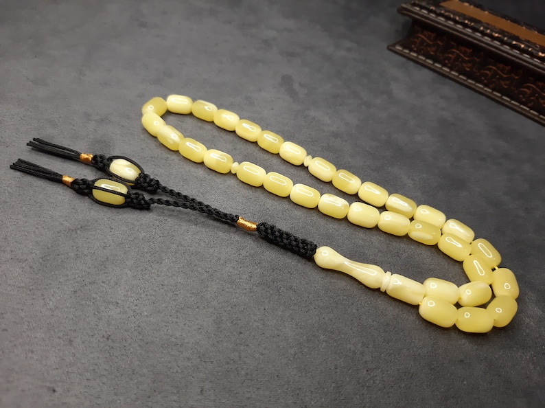 May include: A yellow amber prayer beads necklace with a black tassel and a white bone handle.