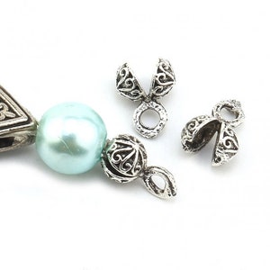 May include: Two silver-toned metal bead caps with an ornate design. The caps are open on one side and have a small loop on the other side.