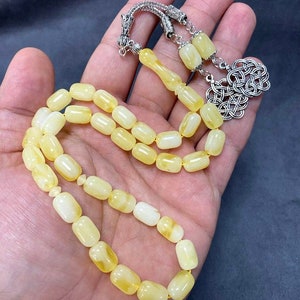 Puede incluir: Un collar de cuentas de oraci&oacute;n de &aacute;mbar amarillo con un cierre de plata. Las cuentas son de forma ovalada y tienen un acabado liso y pulido.