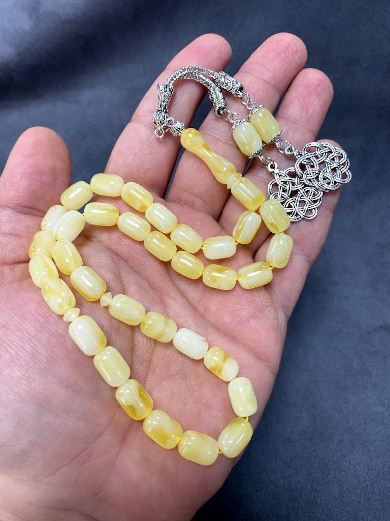 Puede incluir: Un collar de cuentas de oraci&oacute;n de &aacute;mbar amarillo con un cierre de plata. Las cuentas son de forma ovalada y tienen un acabado liso y pulido.