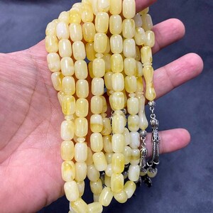 Puede incluir: Un collar de cuentas de oraci&oacute;n de &aacute;mbar amarillo con un borla de plata. Las cuentas son de forma ovalada y tienen un acabado liso y pulido.