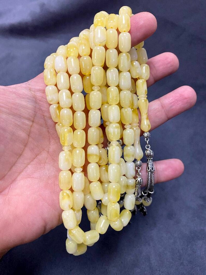 Puede incluir: Un collar de cuentas de oraci&oacute;n de &aacute;mbar amarillo con un borla de plata. Las cuentas son de forma ovalada y tienen un acabado liso y pulido.