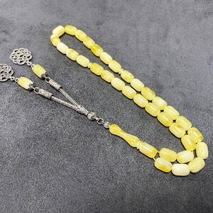 Puede incluir: Un collar de cuentas de oraci&oacute;n de &aacute;mbar amarillo con detalles plateados. Las cuentas son de forma ovalada y el collar tiene un borla.