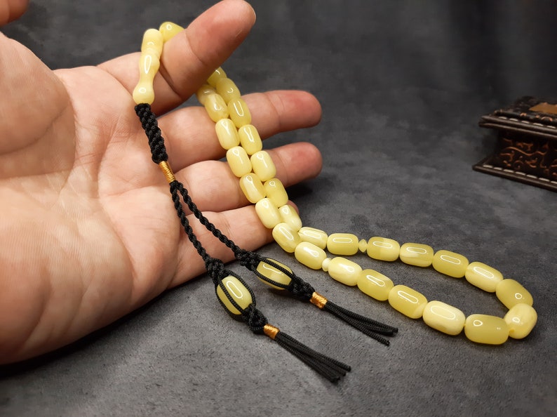 May include: A yellow amber prayer beads necklace with black tassels and gold accents. The beads are oval shaped and strung on a black cord.