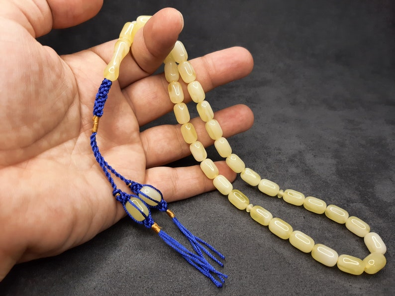 May include: A yellow amber prayer beads necklace with blue tassels. The beads are oval shaped and strung on a thin cord.