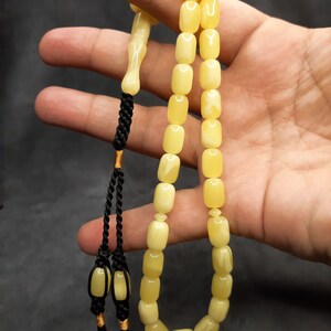 May include: A yellow amber prayer beads necklace with a black tassel. The beads are rectangular and have a smooth, polished finish.