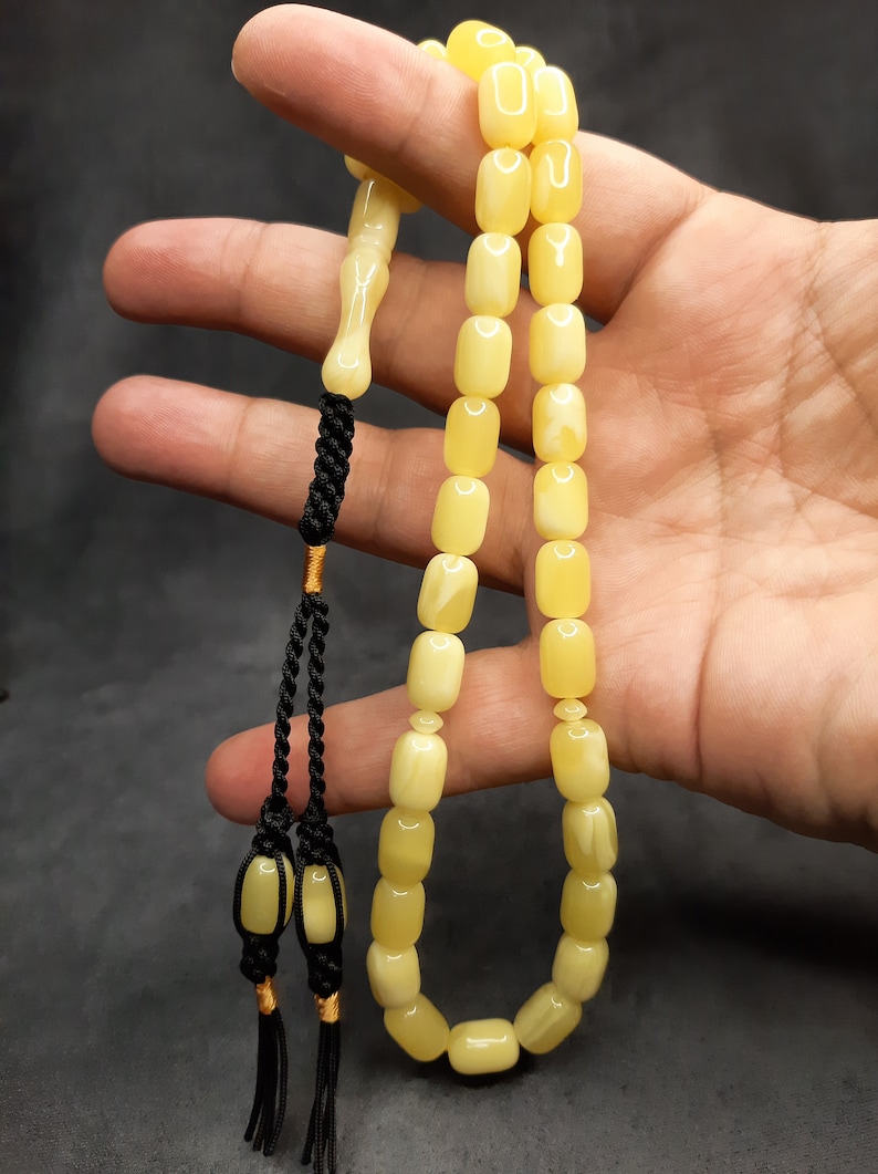 May include: A yellow amber prayer beads necklace with a black tassel. The beads are rectangular and have a smooth, polished finish.