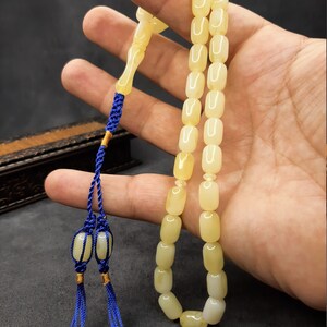 May include: A yellow amber prayer beads necklace with a blue tassel. The beads are rectangular and have a smooth, polished finish.