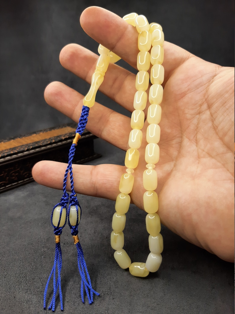 May include: A yellow amber prayer beads necklace with a blue tassel. The beads are rectangular and have a smooth, polished finish.