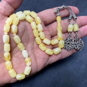 Puede incluir: Un collar de cuentas de oraci&oacute;n de &aacute;mbar amarillo con un borla de plata y un dise&ntilde;o de nudo de plata.