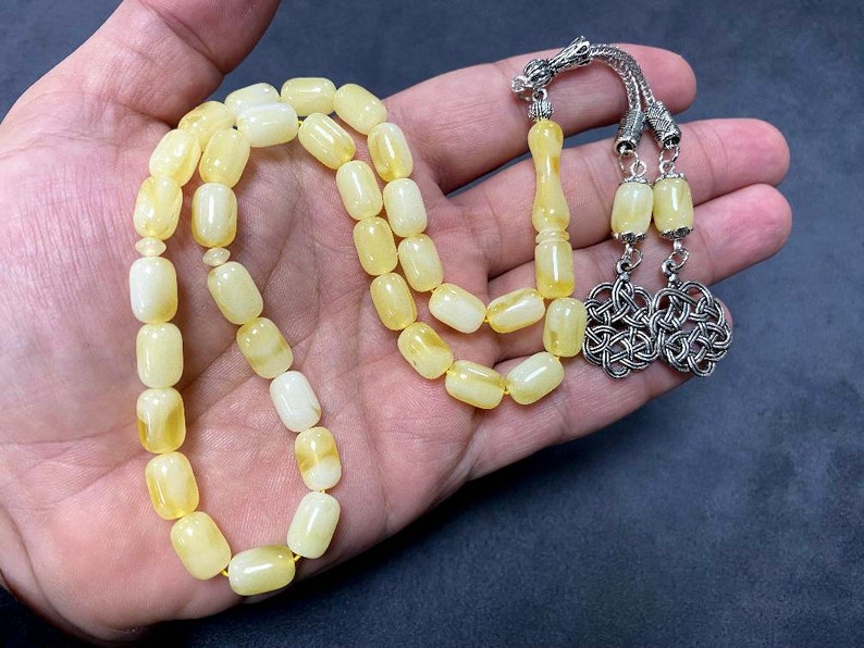 Puede incluir: Un collar de cuentas de oraci&oacute;n de &aacute;mbar amarillo con un borla de plata y un dise&ntilde;o de nudo de plata.