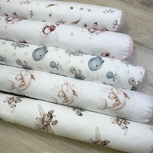 Könnte beinhalten: Mehrere weiße, zylindrische Babybett-Umrandungen mit verschiedenen Mustern. Eines zeigt ein Marienkäfer- und Blumendesign, ein anderes Wale und Oktopusse, und ein drittes einen Bären in einem Flugzeug. Die Umrandungen sind für Babybetten.