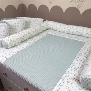 Könnte beinhalten: Eine hellblaue Waffelstruktur-Wickelunterlage mit einem weißen und braunen floralen Muster an der Kante. Die Wickelunterlage liegt auf einer weißen Kommode mit Holzgriffen. Der Text "Antalin Handmade with Love" befindet sich auf der Kante.