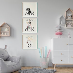 May include: Three framed black and white illustrations of cartoon characters with simple lines and shapes. The illustrations are hung on a white wall above a white dresser with wooden knobs. The dresser has four drawers. A grey armchair with cat ears is in the bottom left corner of the image.