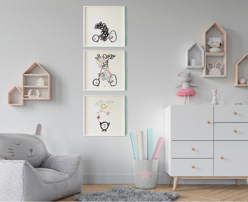 May include: Three framed black and white illustrations of cartoon characters with simple lines and shapes. The illustrations are hung on a white wall above a white dresser with wooden knobs. The dresser has four drawers. A grey armchair with cat ears is in the bottom left corner of the image.