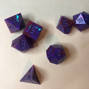 May include: A set of six iridescent purple and red dice with black numbers. The dice are a d4, d6, d8, d10, d12, and d20.