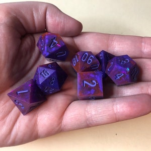 May include: Set of six purple and red dice with white numbers. The dice are made of resin and have a galaxy-like swirl pattern.