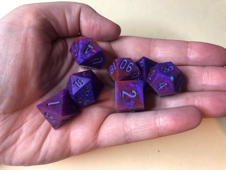 May include: Set of six purple and red dice with white numbers. The dice are made of resin and have a galaxy-like swirl pattern.