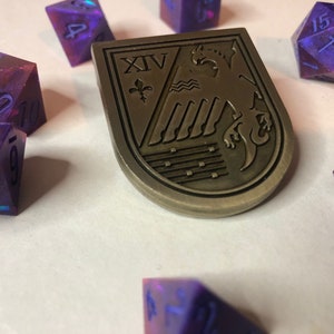 May include: A set of iridescent purple and pink dice with black numbers, a metal shield with a crest and the Roman numeral XIV, and a metal shield with a crest and the Roman numeral XIV.
