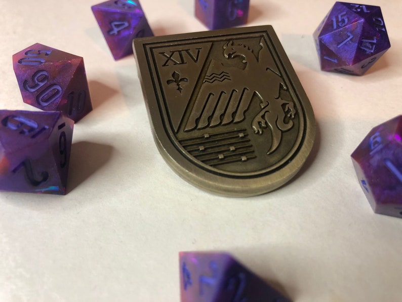 May include: A set of iridescent purple and pink dice with black numbers, a metal shield with a crest and the Roman numeral XIV, and a metal shield with a crest and the Roman numeral XIV.