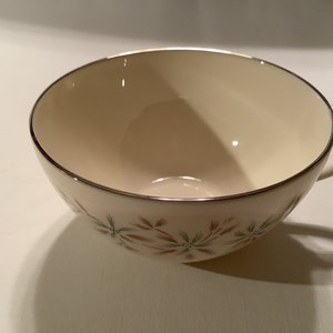 May include: A white ceramic teacup with a gold rim and a floral pattern in shades of brown and blue.