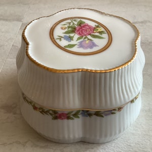 May include: White porcelain trinket box with a scalloped edge and gold trim. The lid features a floral design with pink, purple, and yellow flowers.