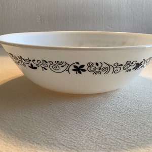 May include: A white ceramic bowl with a black floral design around the rim. The bowl is large and round.