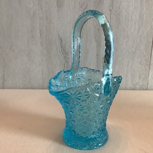 May include: A light blue glass basket with a diamond pattern and a handle. The basket is empty.