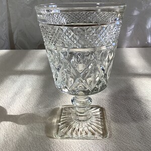 May include: A clear glass goblet with a cut glass design. The goblet has a square base and a round bowl.