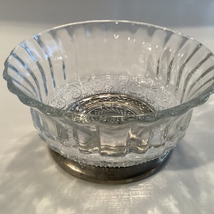 May include: A clear glass bowl with a silver base. The bowl has a scalloped edge and a decorative pattern on the bottom.