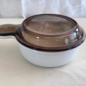 May include: White glass casserole dish with a brown glass lid and a handle. The lid has a slight brown tint.