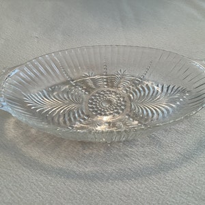 May include: A clear glass serving dish with a scalloped edge and two handles. The dish has a decorative pattern of lines and dots.