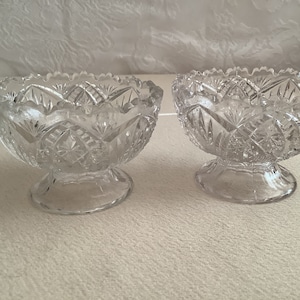 May include: Two clear glass bowls with a cut glass design. The bowls have a pedestal base.