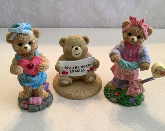 May include: Three teddy bear figurines, each with a different expression and holding a different Valentine's Day themed item. One bear holds a pink heart, another holds a sign that says "You are Beary Special", and the third holds a yellow heart that says "Love".