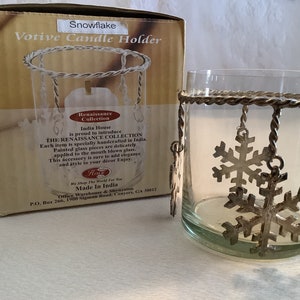 May include: A glass votive candle holder with a silver metal snowflake design. The holder is made in India and is part of the Renaissance Collection. The box reads "Snowflake Votive Candle Holder".