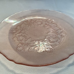 May include: A pink glass plate with a scalloped edge and a floral design.