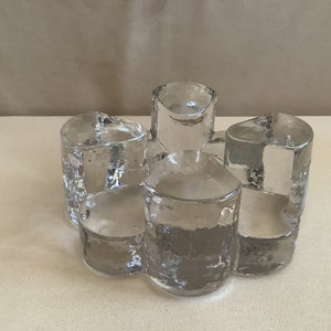 May include: A clear glass candle holder with five individual holders, each with a unique shape and texture. The holder is designed to hold five candles.