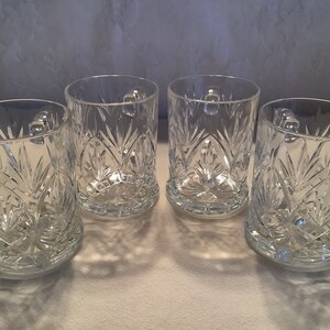 May include: Set of four clear glass mugs with a cut glass design. The mugs have a rounded shape and a handle.