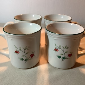 May include: Set of four white ceramic mugs with green trim and a red berry and green leaf design.