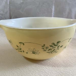 May include: A yellow mixing bowl with a green floral design. The bowl has a white rim and a pouring spout.