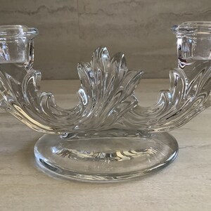 May include: A clear glass candle holder with two candle cups. The holder is designed with a swirling, leaf-like pattern.