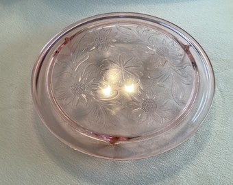 May include: A pink glass cake plate with a floral design and four feet.