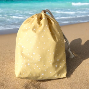 Puede incluir: Una bolsa de cordón amarilla con un patrón de estrellas blancas. La bolsa está hecha de tela y tiene un cierre de cordón.