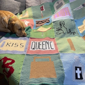 May include: A crocheted blanket with various squares featuring different designs and words, including "KISS", "QUEENIC", and a cross. The blanket is green, blue, pink, and yellow.
