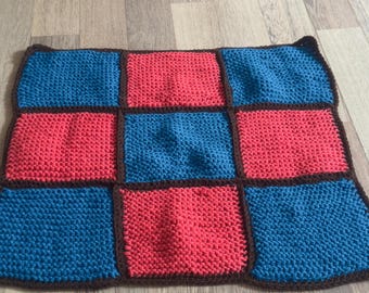 Könnte beinhalten: Handgestrickte quadratische Decke mit Patchwork-Design. Die Decke hat einen dunkelbraunen Rand und ist in neun Quadrate unterteilt. Die Quadrate wechseln sich zwischen einem leuchtenden Türkisblau und einem leuchtenden Korallenrot ab.