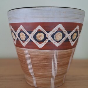 Può includere: Un vaso in ceramica marrone con un bordo bianco e un design geometrico in tonalità di marrone, bianco e nero.