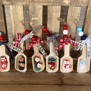 May include: Five wooden spoons decorated for Christmas. Each spoon has a different theme: snowman, fresh baked, Santa, cookies, and it snows. Each spoon has a small figurine, ribbon, and beads.