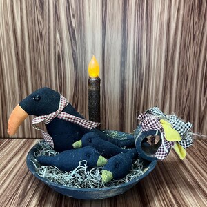 May include: A decorative arrangement featuring a black bowl filled with faux moss and several black bird figures with orange and green accents. A battery-operated candle and a decorative bow complete the rustic, farmhouse-style display.