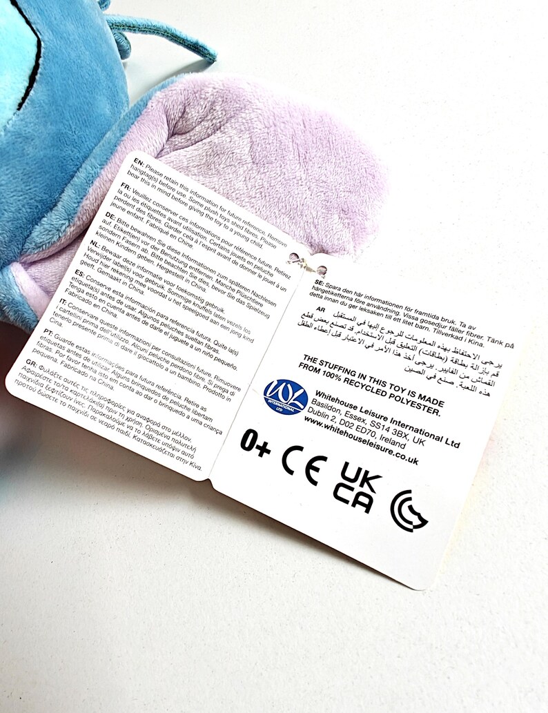 May include: A plush toy with blue and purple sections, with a tag attached. The tag includes text in multiple languages, the toy's stuffing is made from 100% recycled polyester, and the toy is suitable for ages 0+.