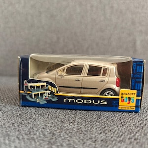 May include: A silver Renault Modus toy car in its original box. The box is blue with the words "MODUS" and "RENAULT TOYS" printed on it. The toy car is a miniature replica of the real vehicle.
